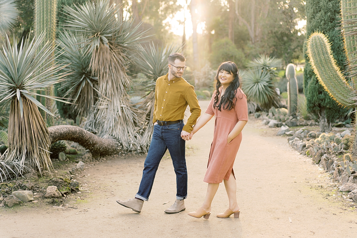 woman in pink dress posing with man in jeans and yellow shirt in arizona cactus gardens, taken by paige vaughn