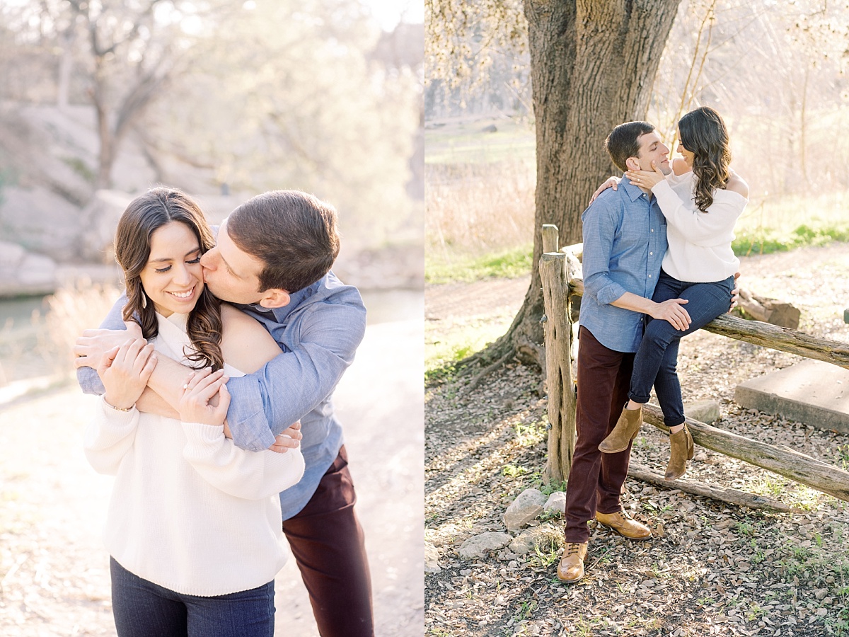 A man in a blue shirt wrap his arms around a pretty woman with long hair and a white sweater and kisses her on the cheek.