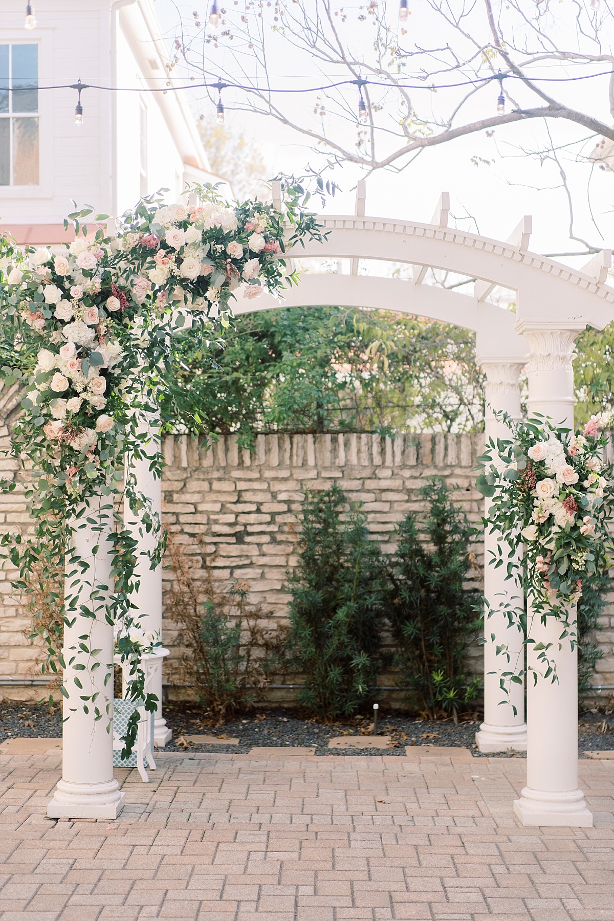 Beautiful white wedding archway covered in greens and blush pink flowers at The Mansion in Austin, Texas.