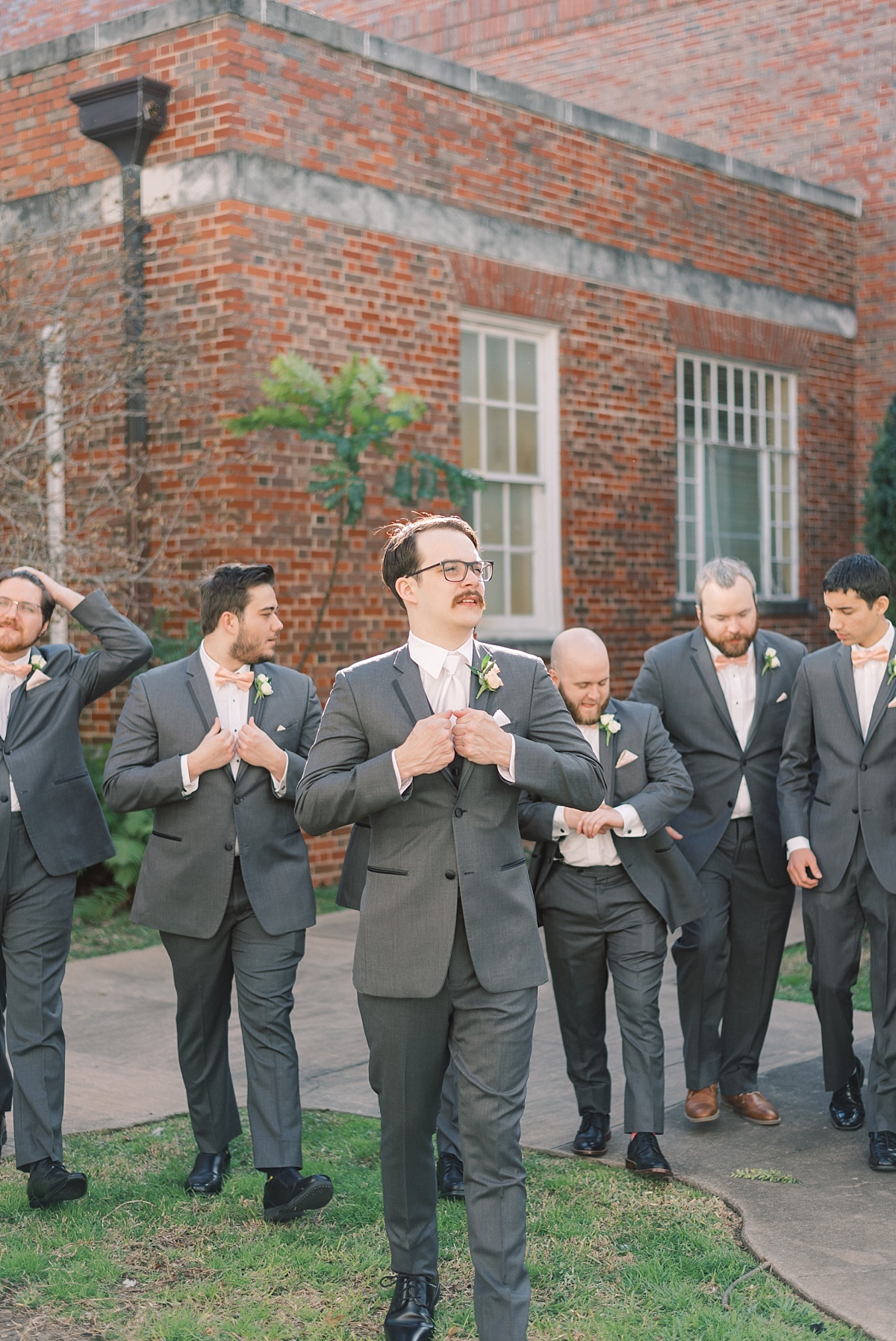 A candid shot by Paige Vaughn Photography of a groom walking with his groomsmen dressed in grey tuxes as they prepare for his wedding day at TFWC Mansion in Austin, Texas.