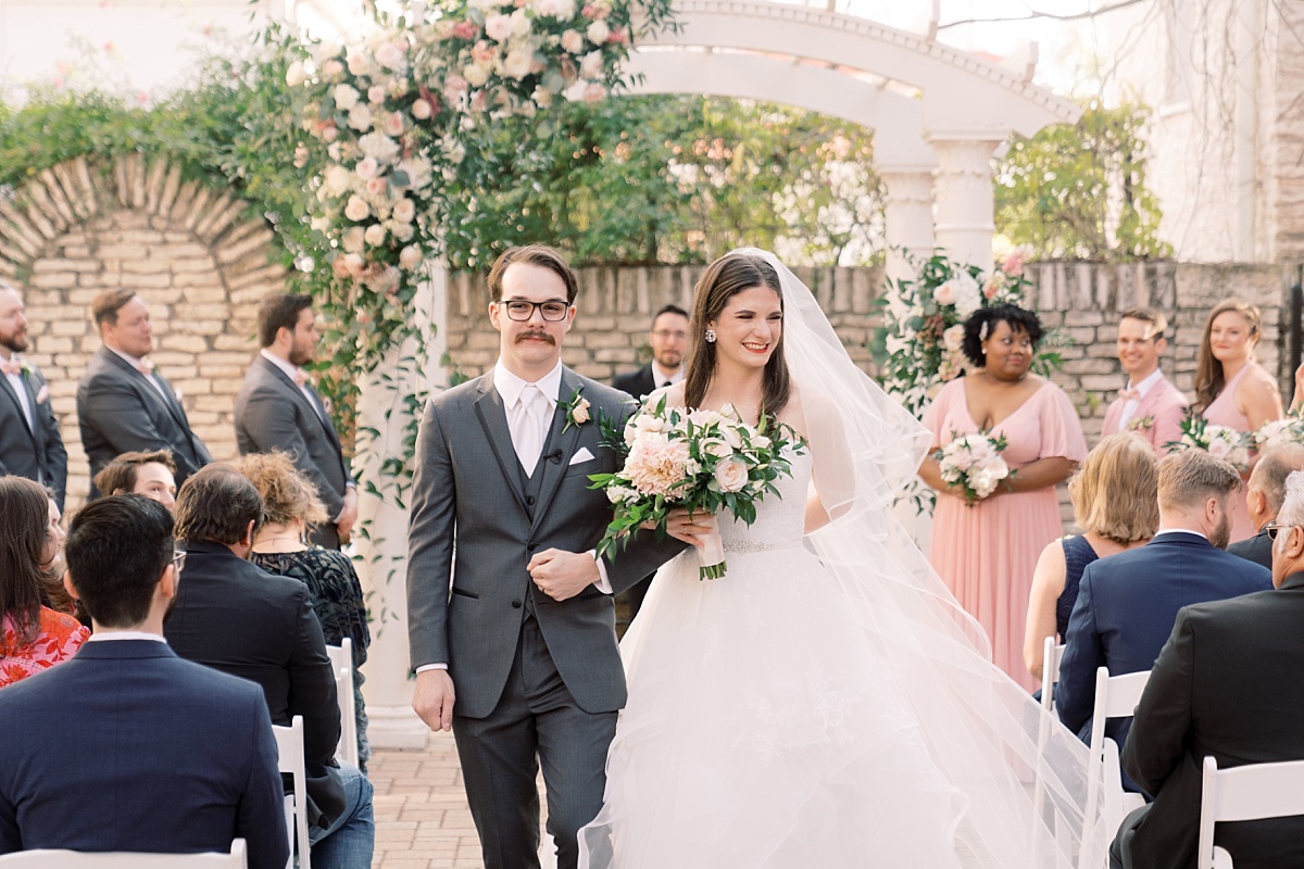 A just-married bride and groom walk up the aisle arm-in-arm while having their photo taken by wedding photographer Paige Vaughn in Austin, Texas.