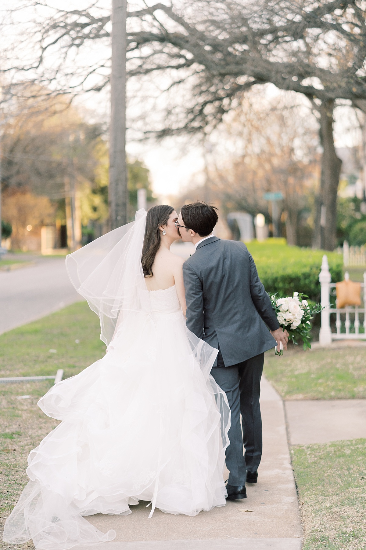 A bride and groom kiss while walking away from the camera on a quaint street in Austin, Texas while Paige Vaughn takes their wedding photos.