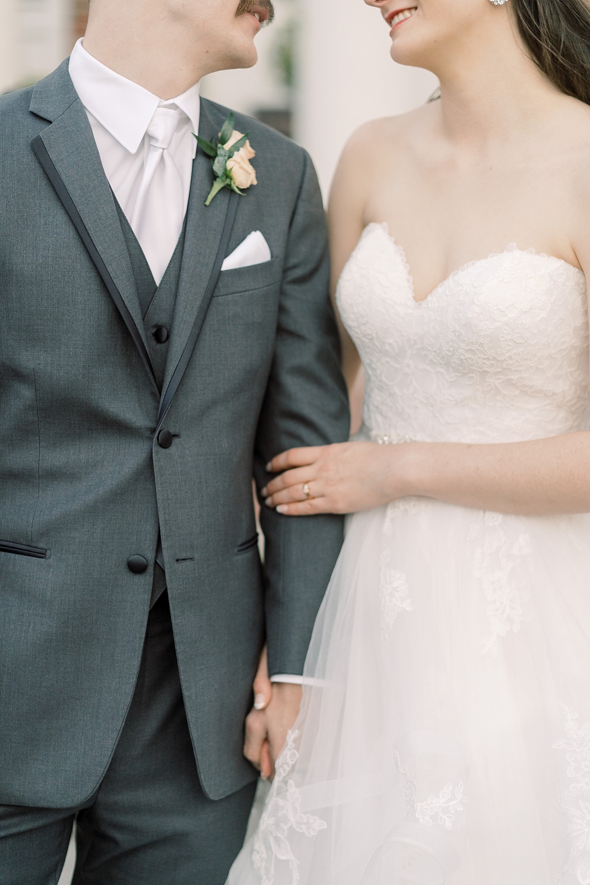 A close up image of a bride in a white dress and groom in a gray tux holding hands and smiling at each other for wedding photographer in Austin, Texas.