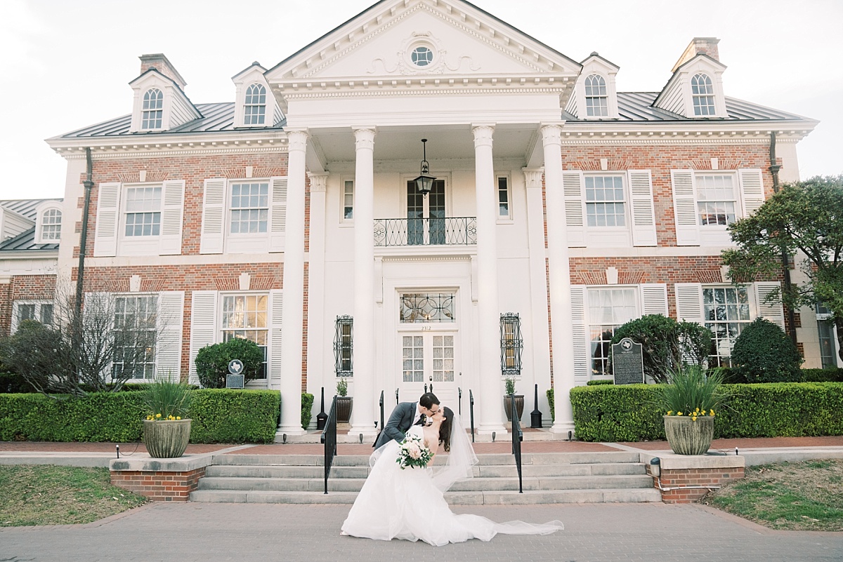 A groom dips and kisses his bride in front of The Mansion while having romantic wedding photos taken by Paige Vaughn Photography in Austin, Texas.