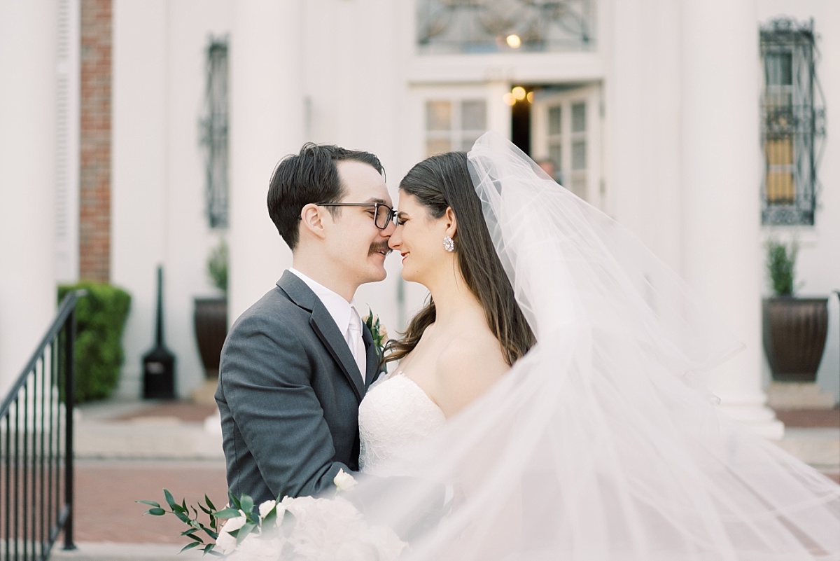 A groom in a gray suit and bride wearing a long, white veil about to kiss on their wedding day at The Mansion in Austin, Texas.