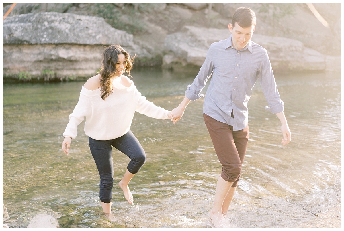 A happy couple holds hands while walking barefoot through the Colorado River for their engagement photos in Austin, Texas. Austin marriage proposal, downtown Austin proposal, Austin proposal photographers, Austin proposal photographer, engagement photos in downtown austin, downtown austin engagement photos, awesome engagement photos in austin, downtown austin photo spots, austin engagement photos, engagement session in austin, austin engagement session, austin wedding photographer, austin wedding photos, wedding photos in austin, colorful austin photographer, fine art austin photographer, fine art austin wedding photographer, wedding photographer in austin, austin wedding ideas, engagement photo ideas in austin