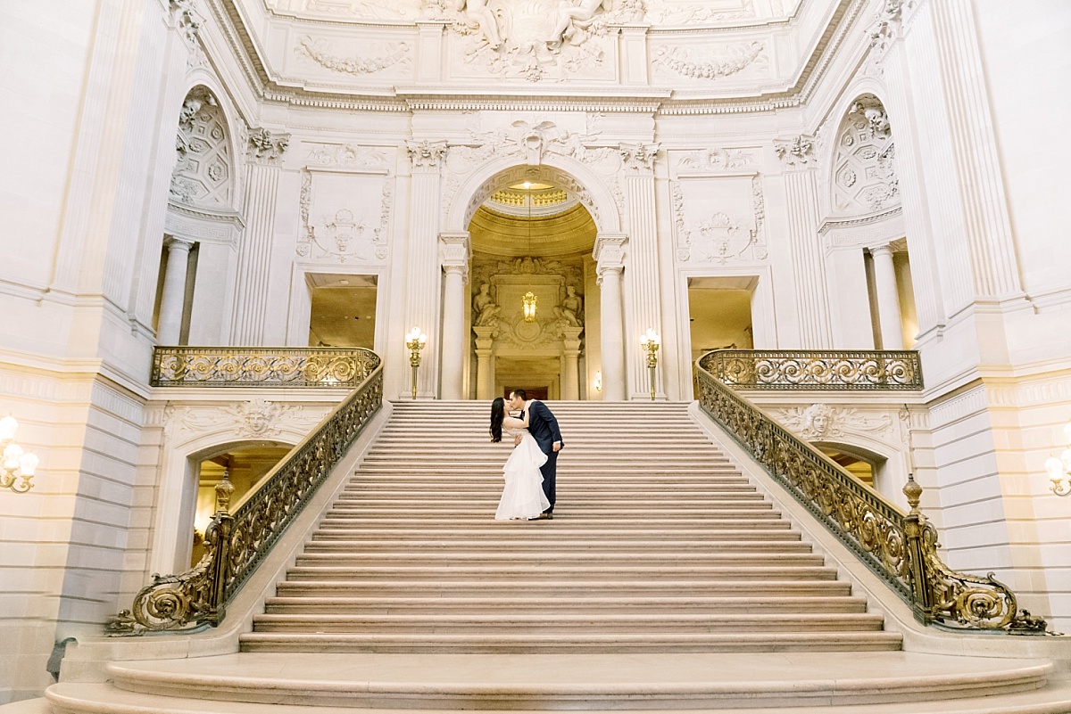Newlywed couple standing on the stairs of gorgeous San Francisco City Hall and kissing for their wedding photos with Paige Vaughn Photography