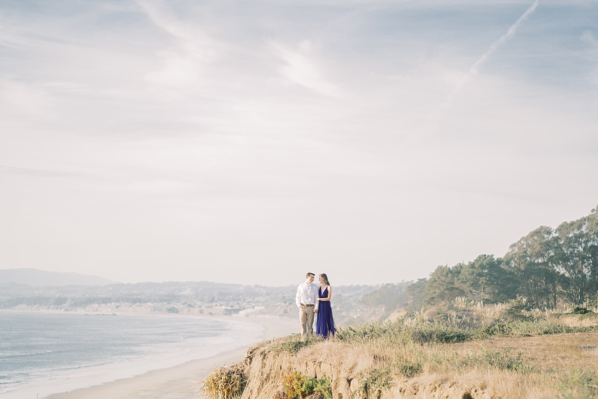 Attractive couple stands together on a cliff overlooking a beautiful seashore at La Selva Beach, California for engagement photos with Paige Vaughn Photography