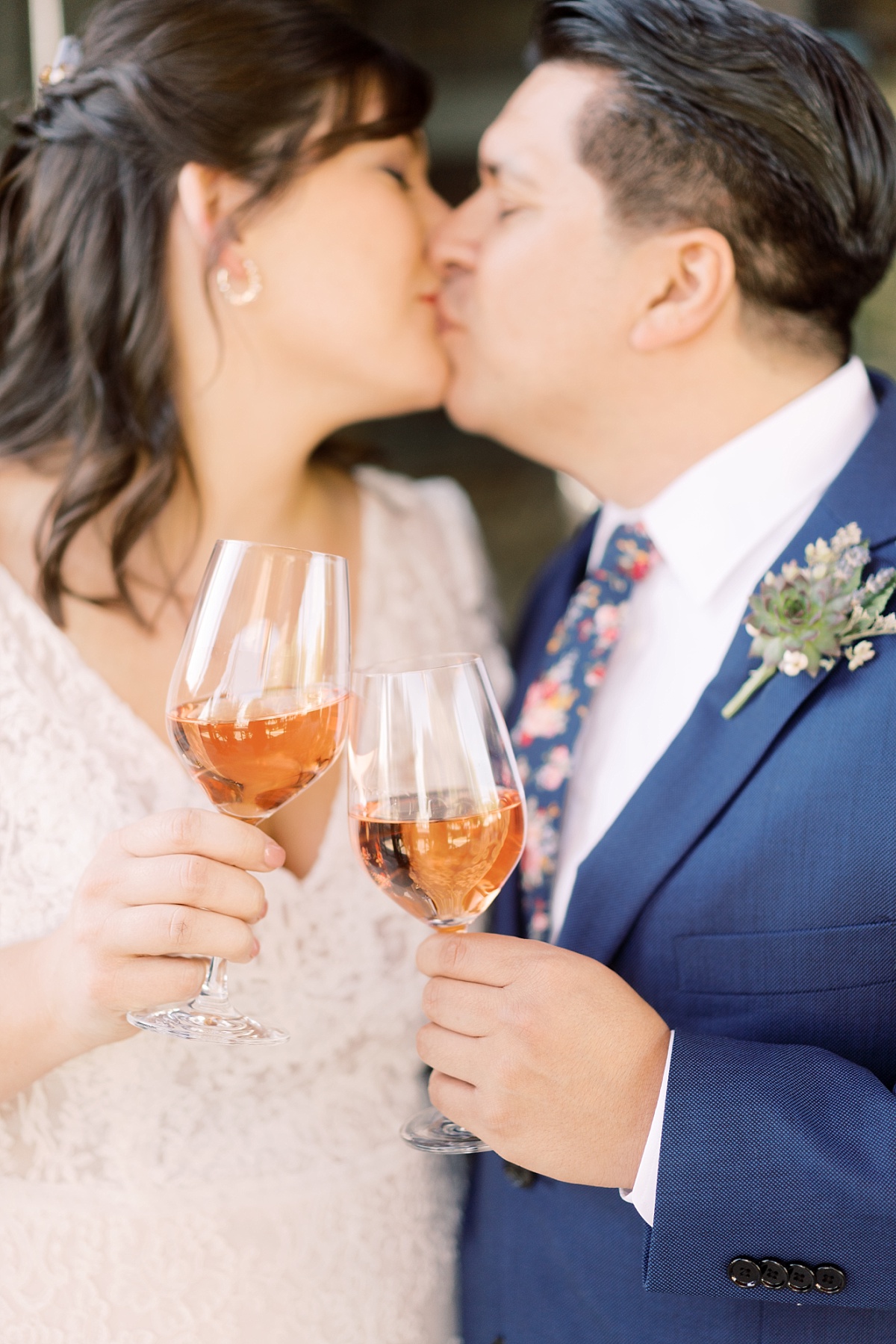 Couple kisses while holding glasses of wine during intimate wedding celebration