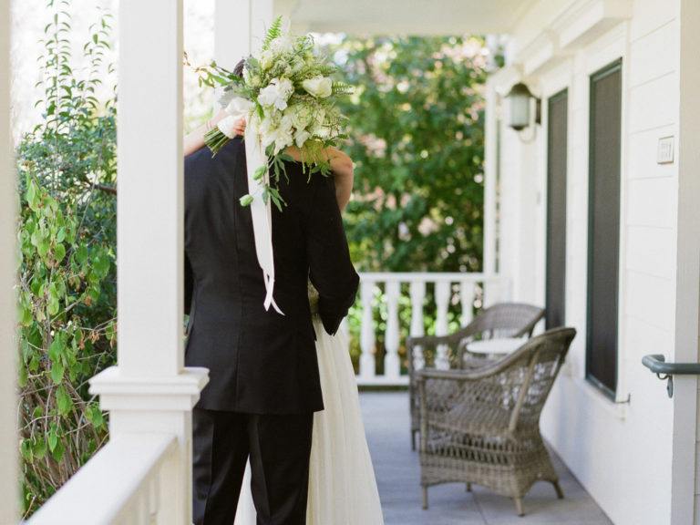 A newlywed couple kisses on an elegant, white farmhouse-style porch at MacArthur Place, an excellent Bay Area outdoor wedding venue