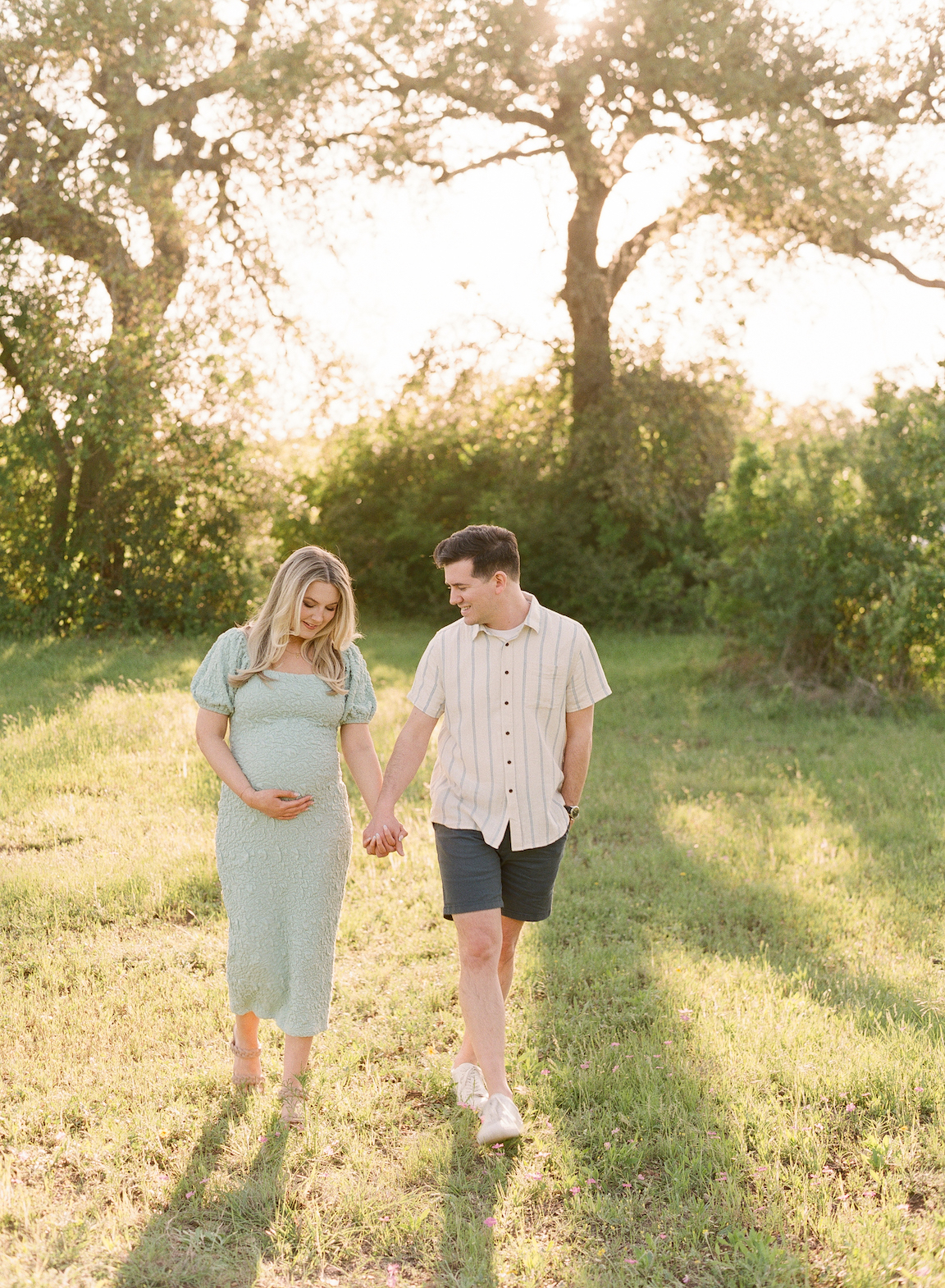 expecting parents walking hand in hand in a sunshine park for their maternity photos