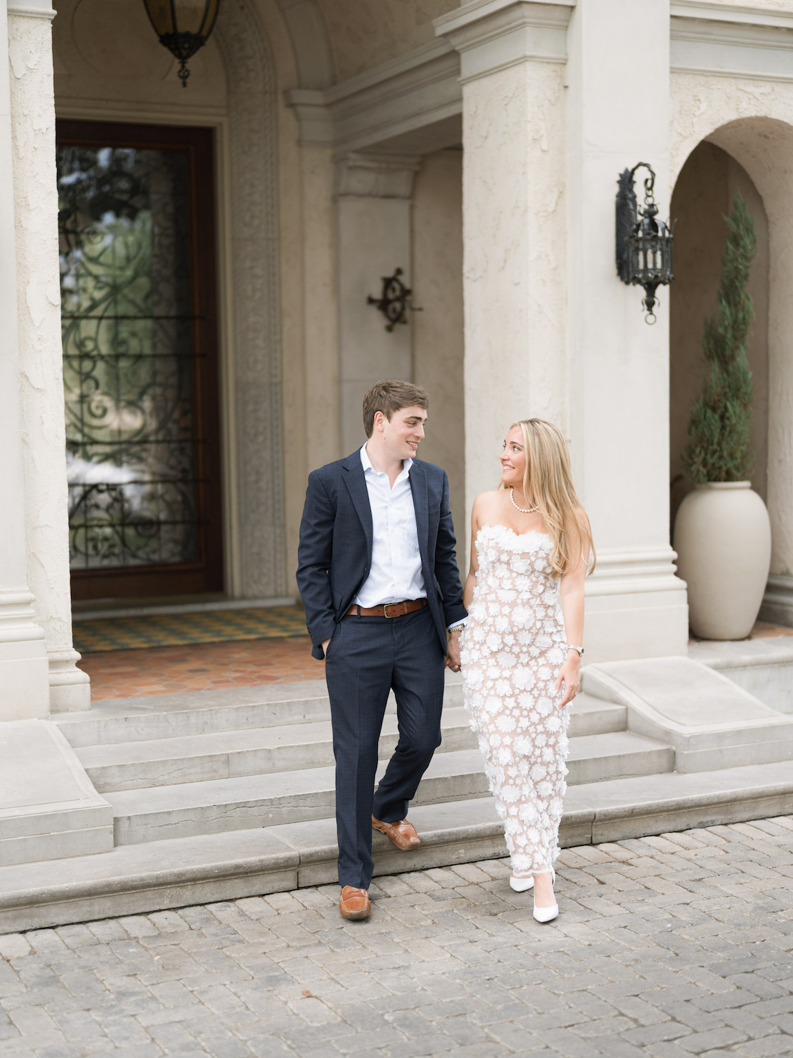 Engaged couple walking through the elegant gardens of Commodore Perry Estate, captured on film with soft natural light and classic architecture in the background