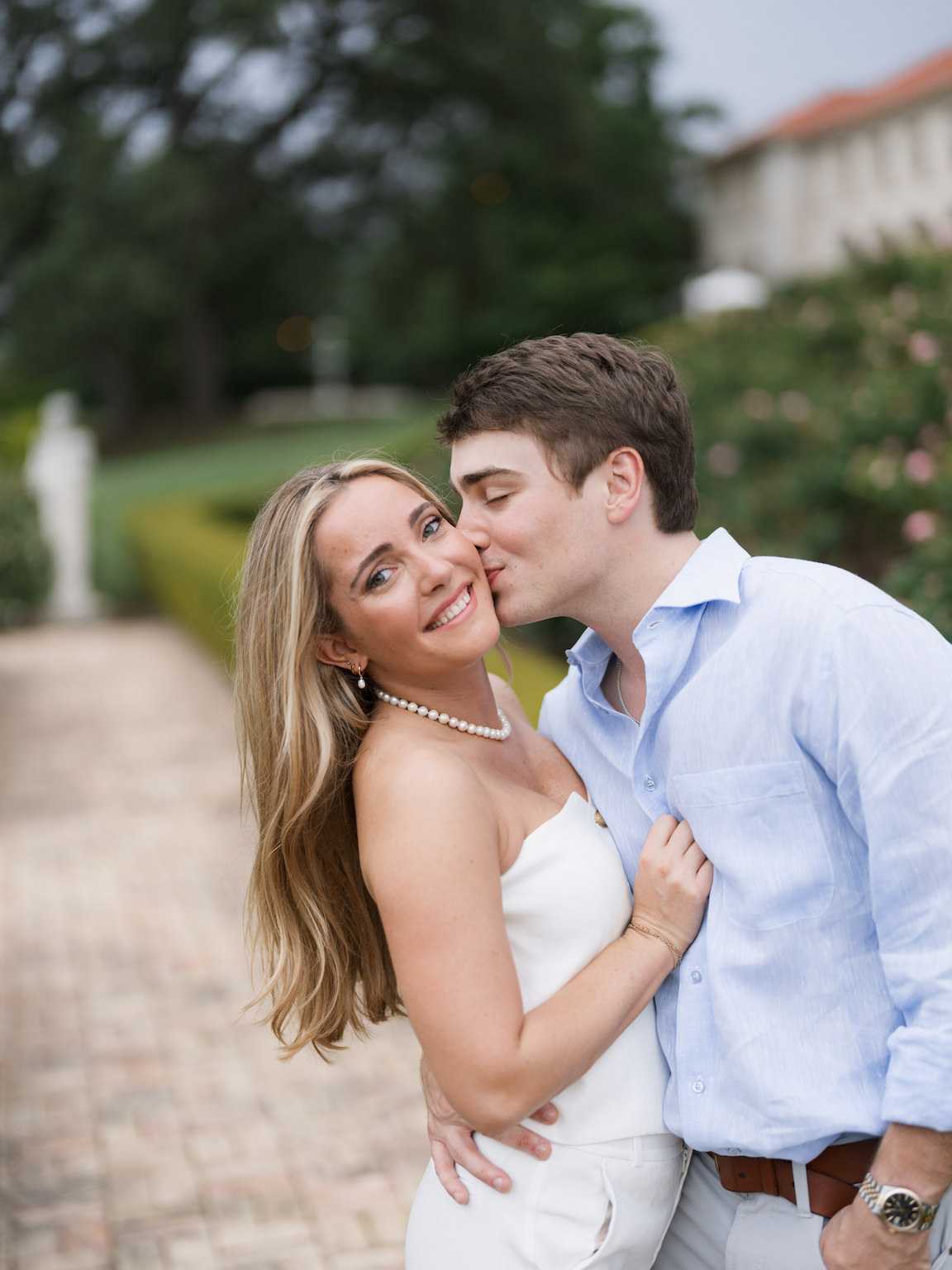 Engaged couple walking through the elegant gardens of Commodore Perry Estate, captured on film with soft natural light and classic architecture in the background