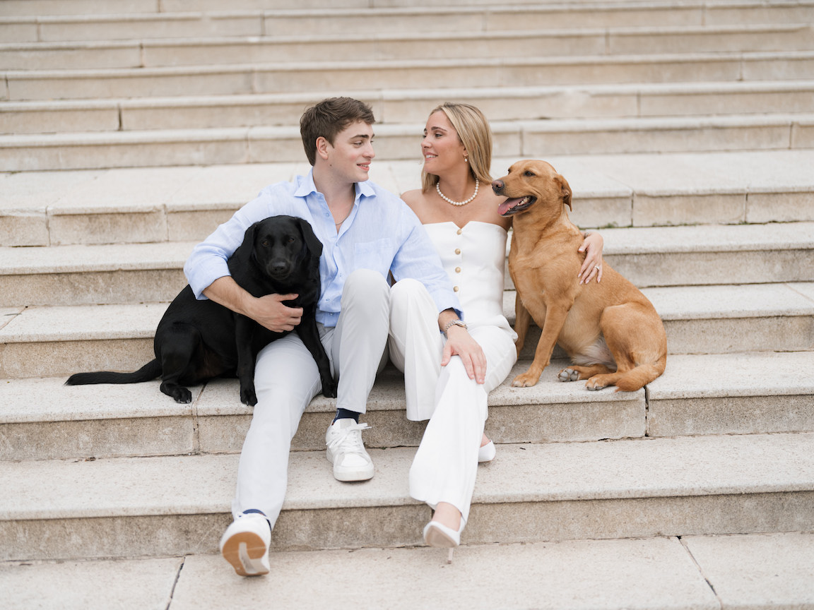 Engagement photo of couple cuddling with their dogs on the lawn of Commodore Perry Estate