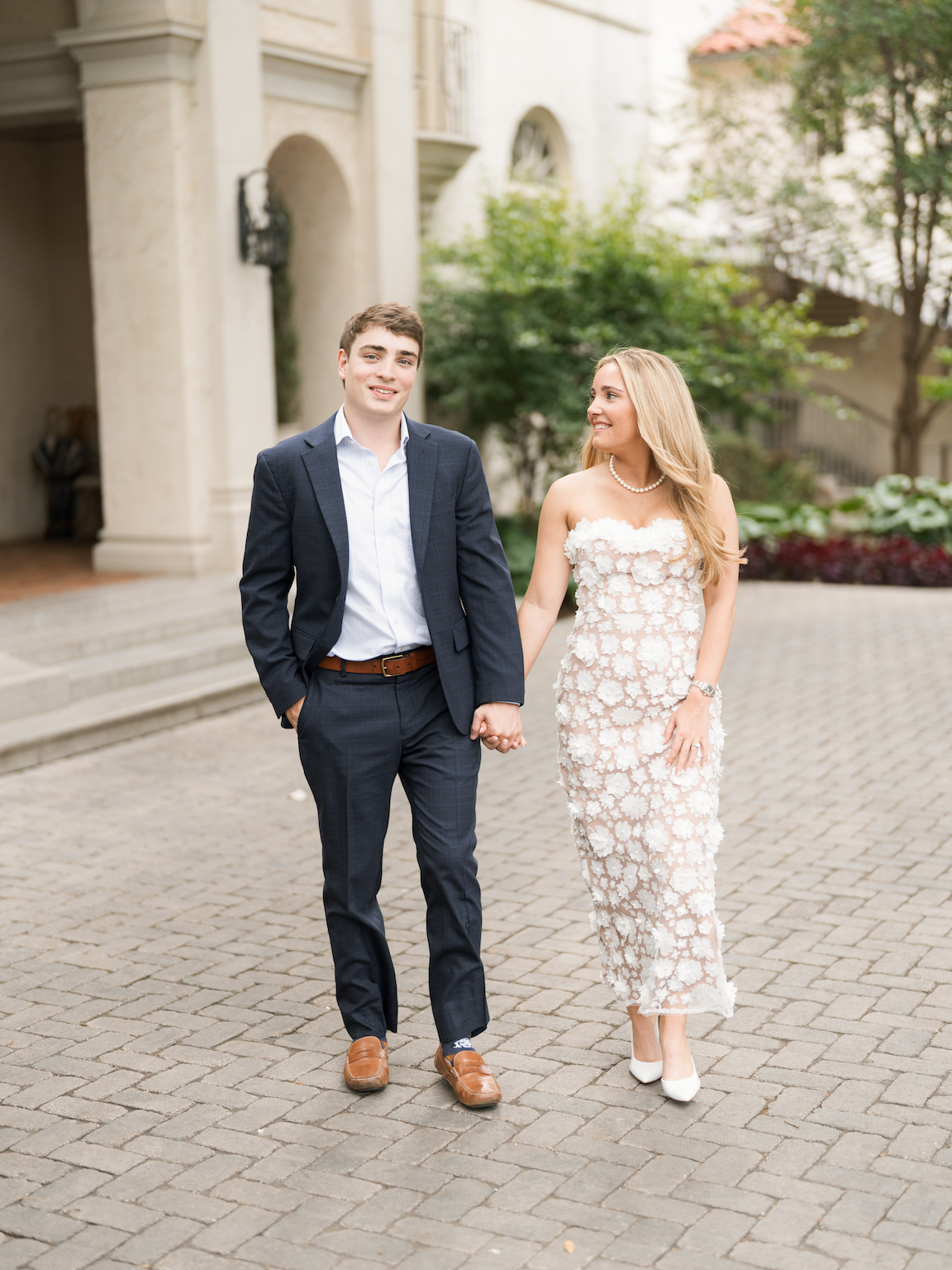 Engaged couple walking through the elegant gardens of Commodore Perry Estate, captured on film with soft natural light and classic architecture in the background