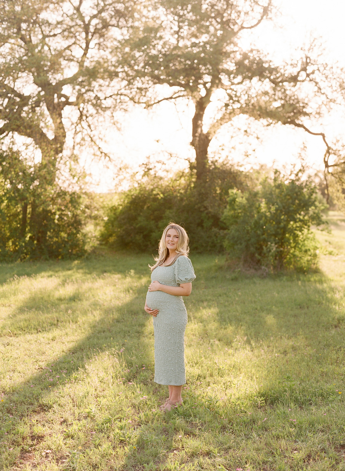 Expecting mother in a grassy field, photographed on film with glowing natural light