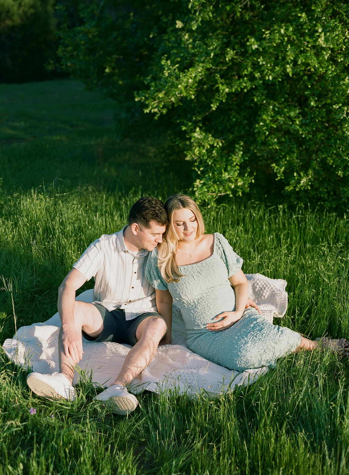 Chelsea and Clayton during their film maternity photos in a sun-drenched Austin park, surrounded by greenery