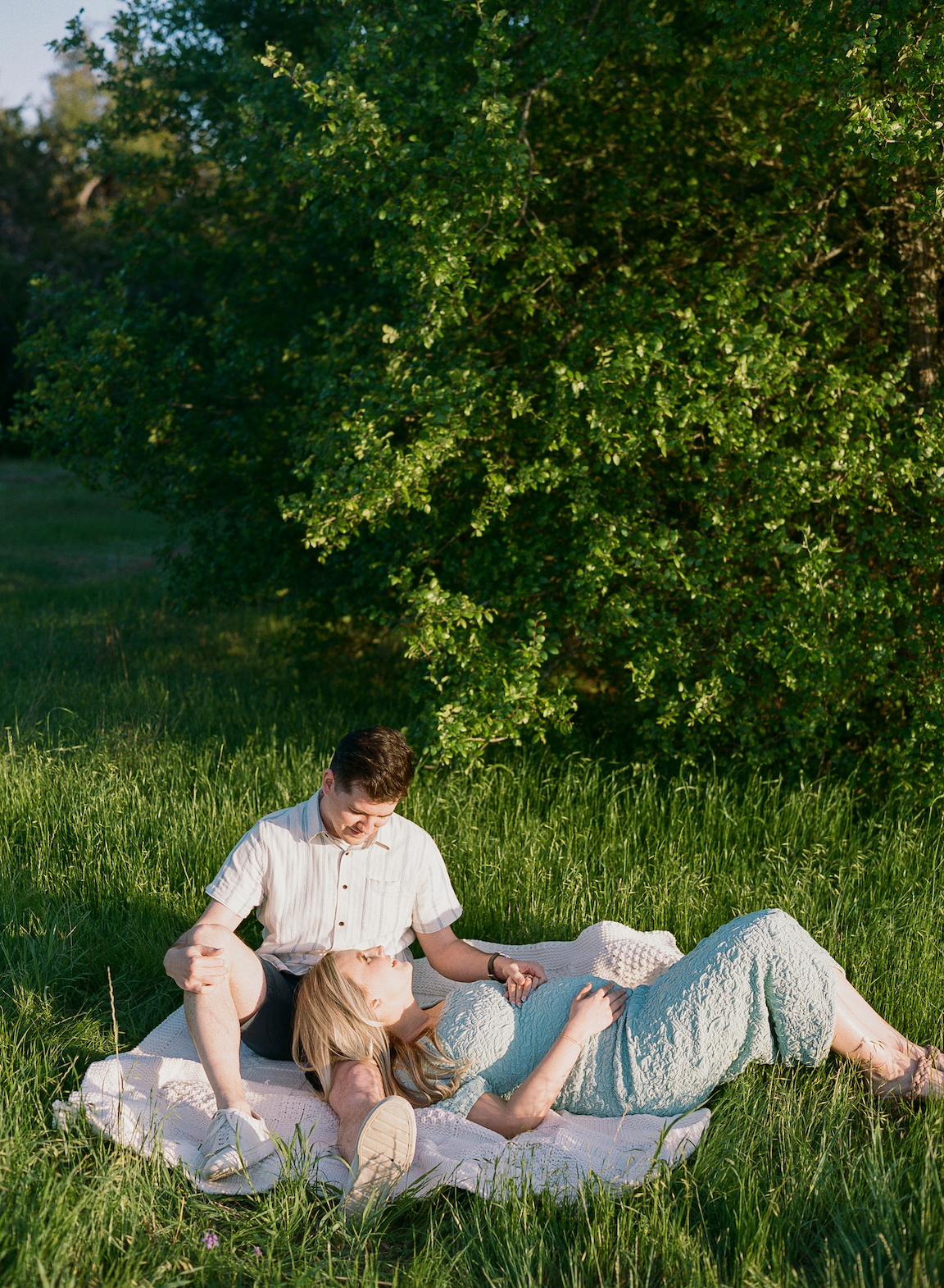 Chelsea and Clayton during their film maternity photos in a sun-drenched Austin park, surrounded by greenery