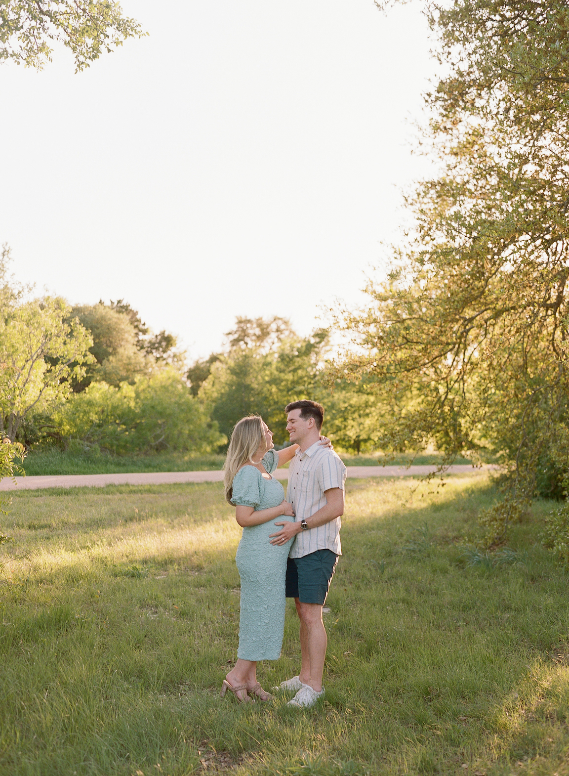 Chelsea and Clayton during their film maternity photos in a sun-drenched Austin park, surrounded by greenery