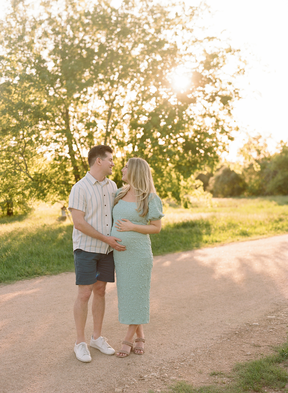 Chelsea and Clayton during their film maternity photos in a sun-drenched Austin park, surrounded by greenery