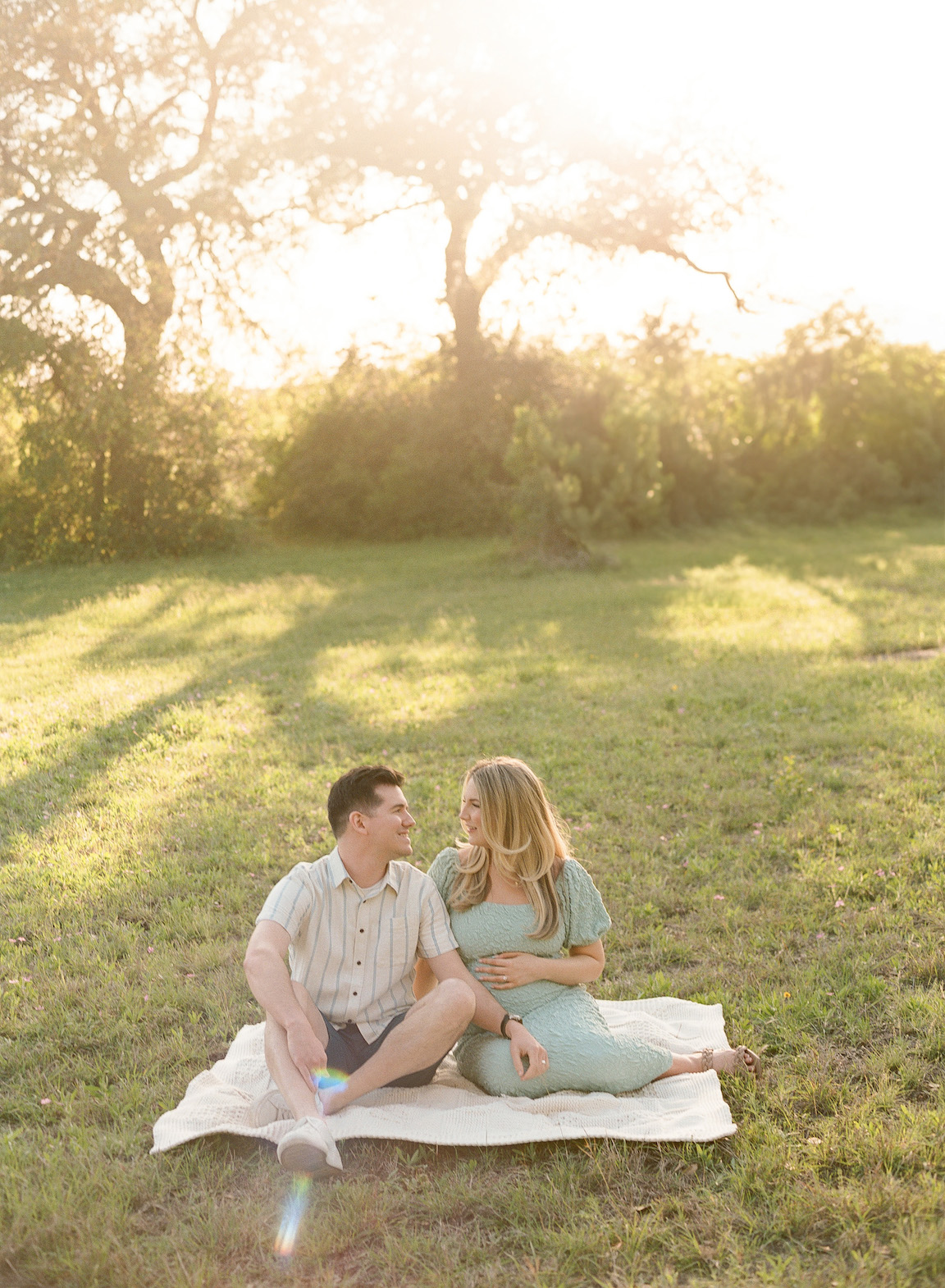 Chelsea and Clayton during their film maternity photos in a sun-drenched Austin park, surrounded by greenery