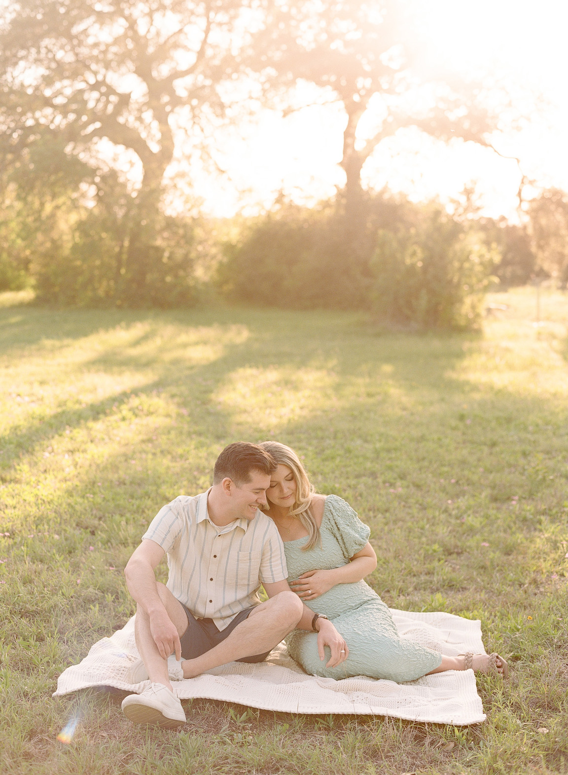 Chelsea and Clayton during their film maternity photos in a sun-drenched Austin park, surrounded by greenery