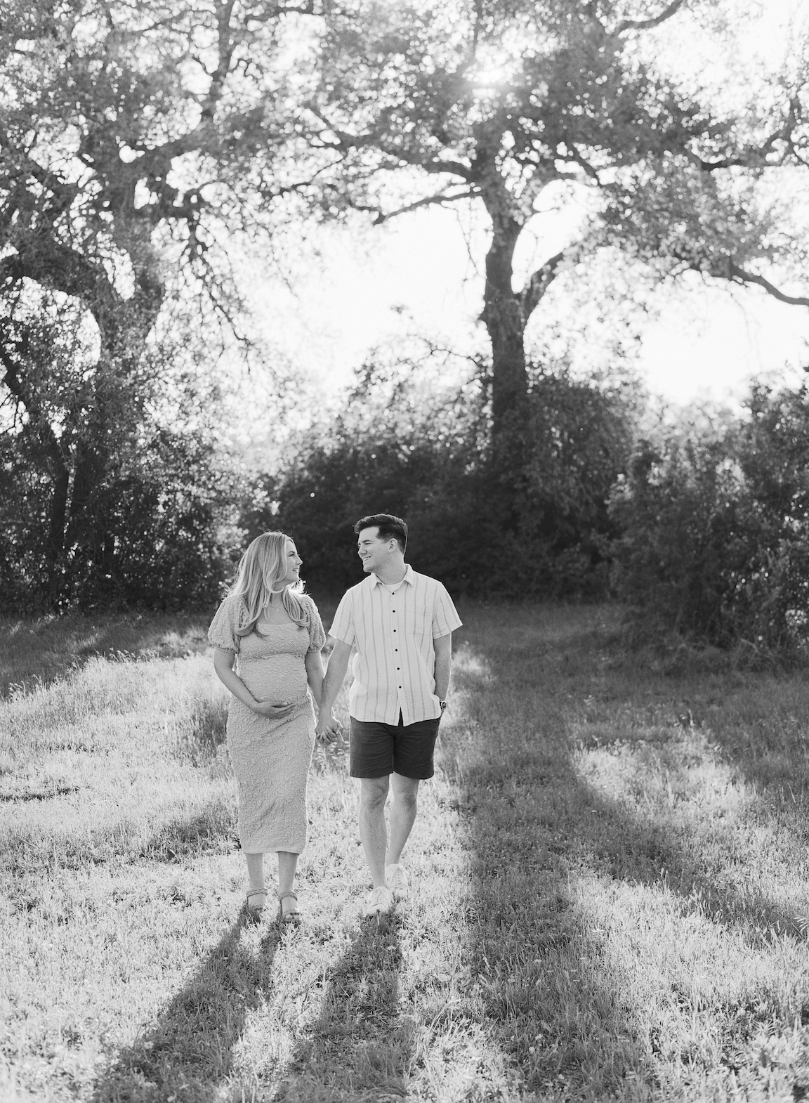 Golden hour film maternity photo of a couple embracing outdoors with soft sunlight filtering through the trees